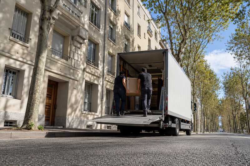 Camion de déménagement, hayon déployé, devant un immeuble des années trente