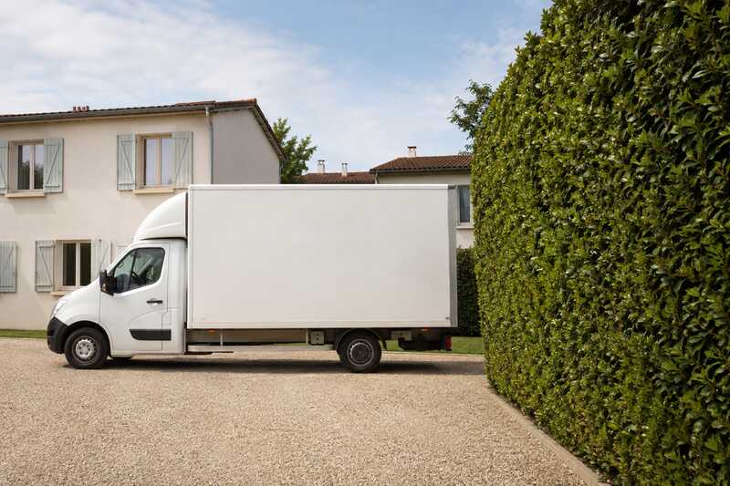 Camion de déménagement reculant dans l’allée gravillonnée d’une maison de faubourg