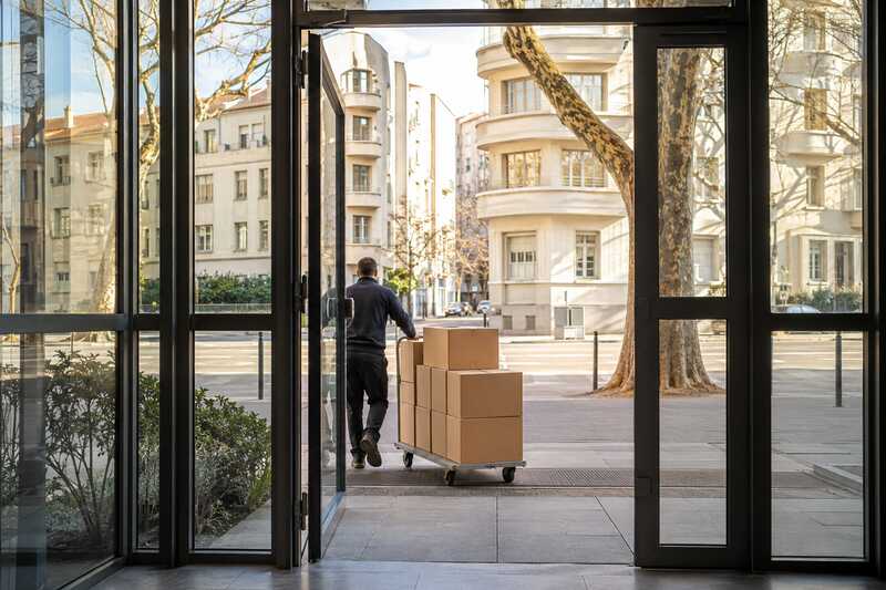 Chariot chargé de cartons sortant du hall vitré d’un immeuble