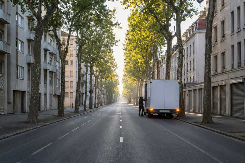Camion à l’arrêt sur une avenue bordée de platanes en début de journée