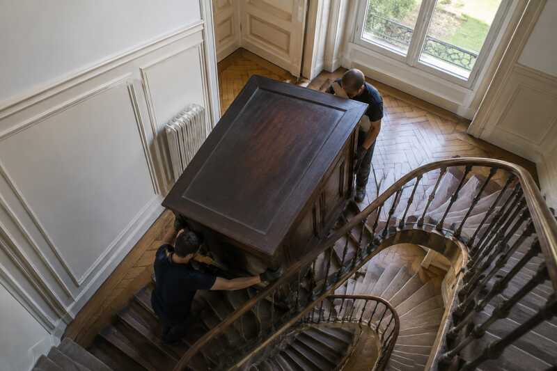Armoire massive guidée dans un escalier étroit par deux déménageurs